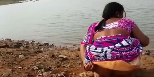 Indian woman peeing in the dirt by a lake