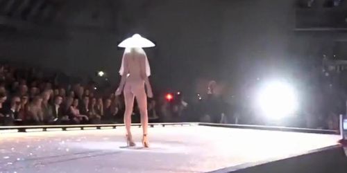 Seductive fashion model in a weird hat walks down the catwalk in the nude